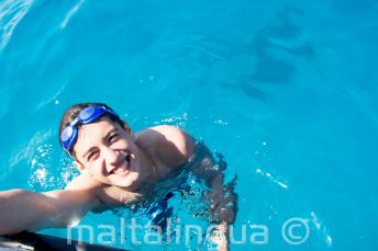 Uno studente che nuota vicino alla barca a Comino.